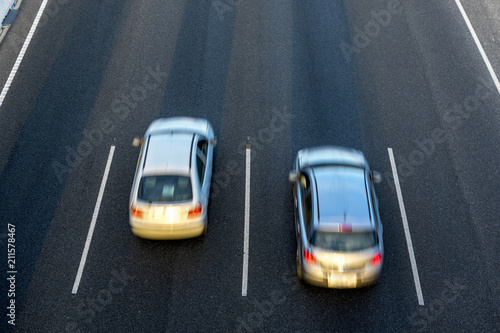 Top view of two cars run fast by the highway, in different lanes in the same direction. Long Exposure.