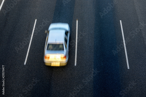 White car runs fast by the third lane of the highway at sunset. Top view and copy space in the other lanes.