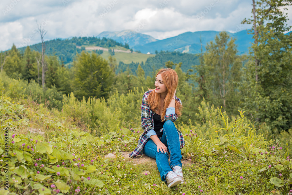 Cheerful woman is having rest on the edge of the cliff and looking at the valley and mountains. Traveling along the mountains, freedom and active lifestyle concept Cheerful woman is having rest on the edge of the cliff and looking at the valley and mountains. Traveling along the mountains, freedom and active lifestyle concept