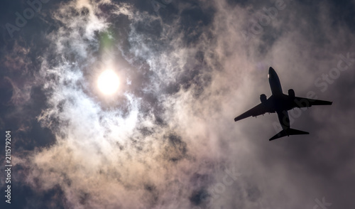 The plane flies in the sky against the sun. 