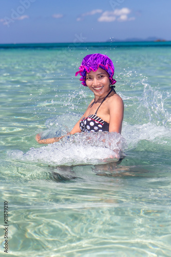 Cheerful woman in retro swimsuit and bathing cap squirts water in a transparent sea. Tropical vacation.