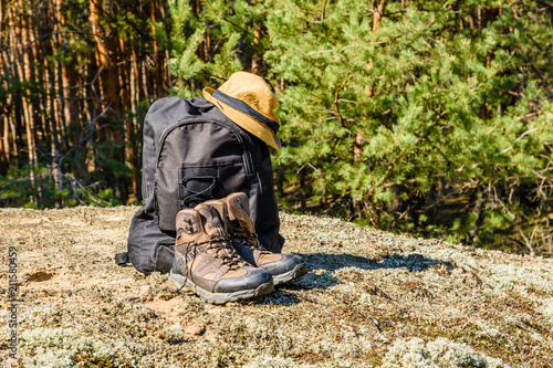 Backpack, touristic boots and hat on a ground in a coniferous forest