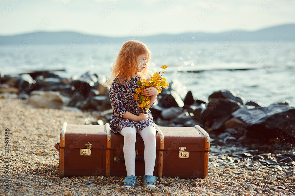 A little sad girl with a toy sitting on a big suitcase near the Stock-Foto  | Adobe Stock