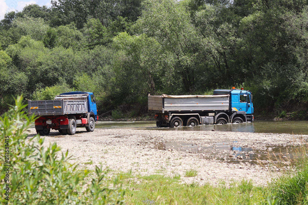 Crossing a trucks through a shallow mountain river. Transportation of goods in hard-to-reach places and dangerous conditions. Ecology of the environment. Rest over the water. The river is a region