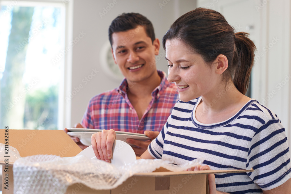Young Couple Unpacking Boxes In Kitchen On Moving Day Young Couple Unpacking Boxes In Kitchen On Moving Day