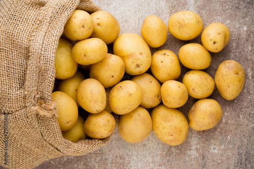 Sack of fresh raw potatoes on wooden background, top view.