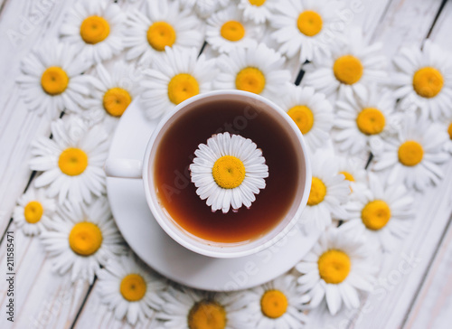 Cup of beauty chamomile tea with fresh daisies. White fresh flowers on a gray vintage wooden background. Top view, close up.