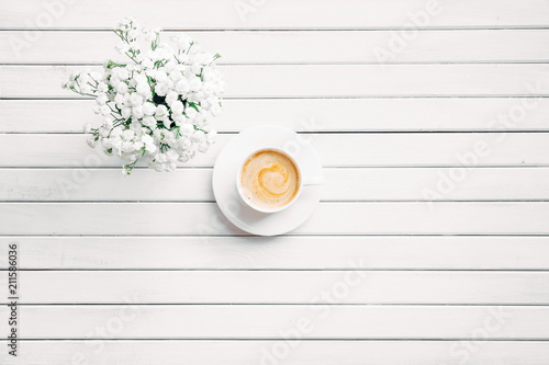 Morning. Cup of coffee on a wooden white background and white flowers. Flat lay, top view, copy space 