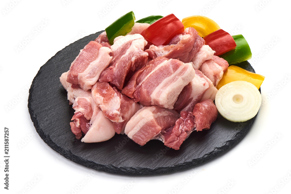 Pieces of fresh pork meat sliced vegetables on stone plate, isolated on white background. Close-up.