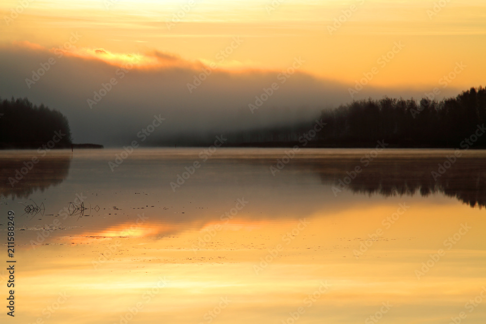 Sun rise colours the sky orange. Lake reflects the same colour.