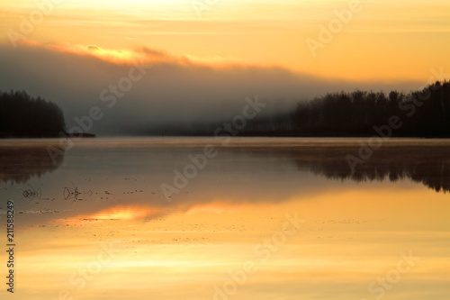 Sun rise colours the sky orange. Lake reflects the same colour. © puteli