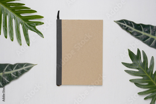 Brown cover notebook on white wooden background with Tropical monstera leaves. Summer and spring concept, Minimal flat lay, Top view.