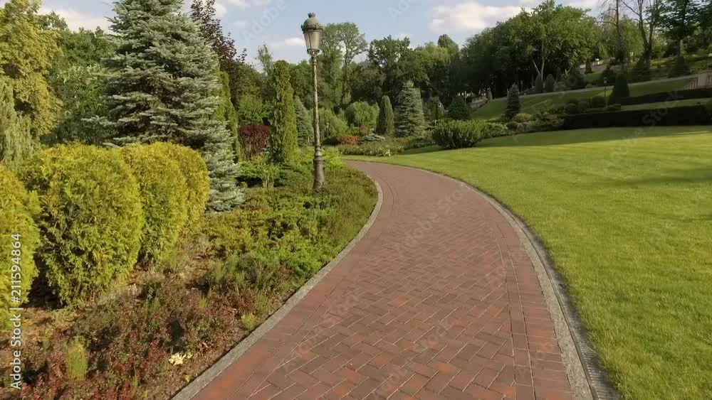 A winding path in a beautiful green formal garden. Park with flowers and trees. Relax and take a walk in nature and fresh air. The camera moves along the track