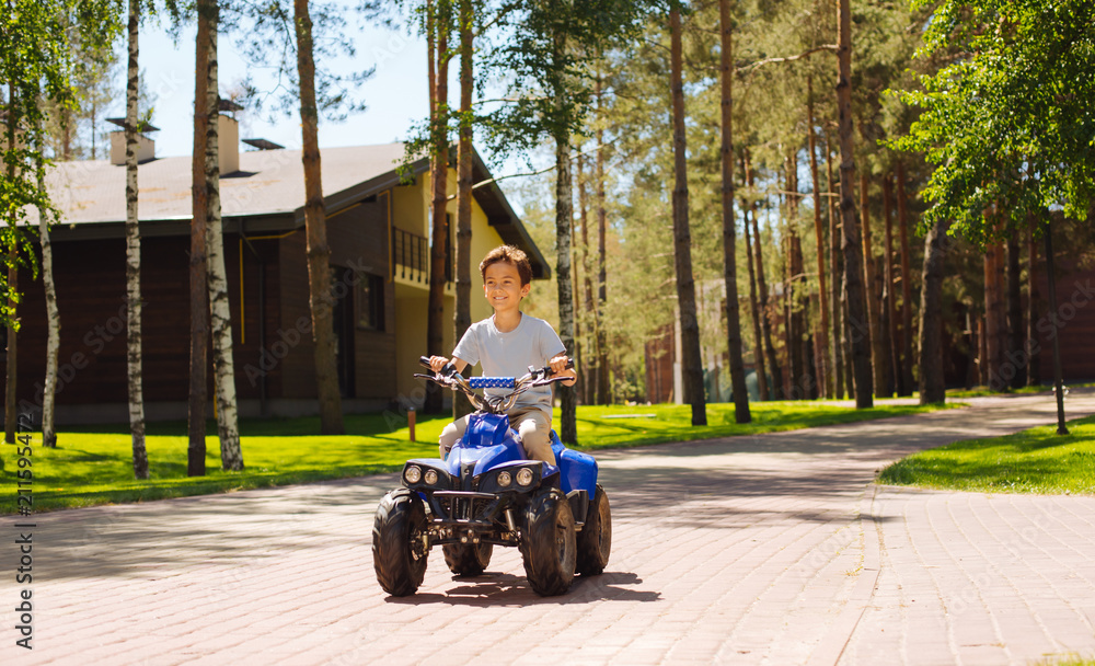 Best driver. Inspired dark-haired schoolboy smiling and driving an ATV Best driver. Inspired dark-haired schoolboy smiling and driving an ATV