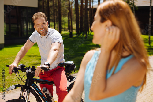 Happy life. Cheerful man riding a bike while looking at his wife and resting outdoors