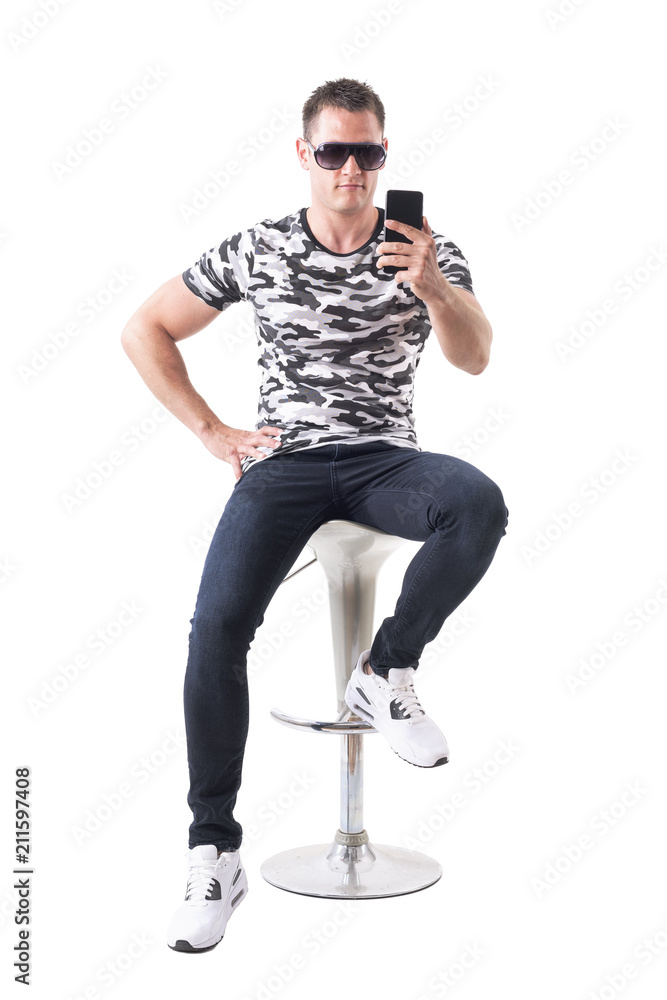 Handsome guy with sunglasses sitting on bar stool taking photo with smart phone. Full body isolated on white background. Handsome guy with sunglasses sitting on bar stool taking photo with smart phone. Full body isolated on white background.