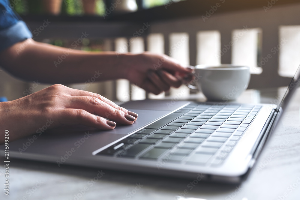 Closeup image of a woman working and typing on laptop keyboard while drinking coffee in office Closeup image of a woman working and typing on laptop keyboard while drinking coffee in office