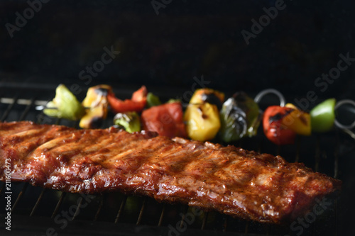 rack of barbecue spare ribs,rack of barbecue spare ribs cooking on a BBQ with green and red peppers, dark background for copy space 