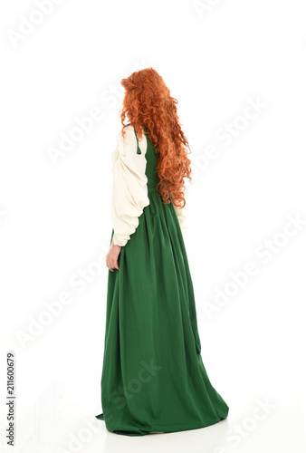 full length portrait of red haired girl wearing long green gown,. standing pose with back to the camera, isolated on white studio background.