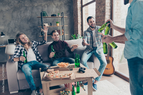 Cropped view of visitor bringing bottles with beer to his stylish, successful, attractive friends with modern hairstyle who extremely happy, glad to see him, having snacks, chips on the table