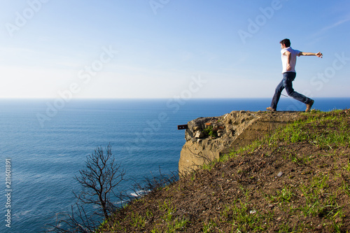 Young man approaches cliff edge by Cantabrian Sea on the coast of Biscay. Risk, dare, attempt concepts