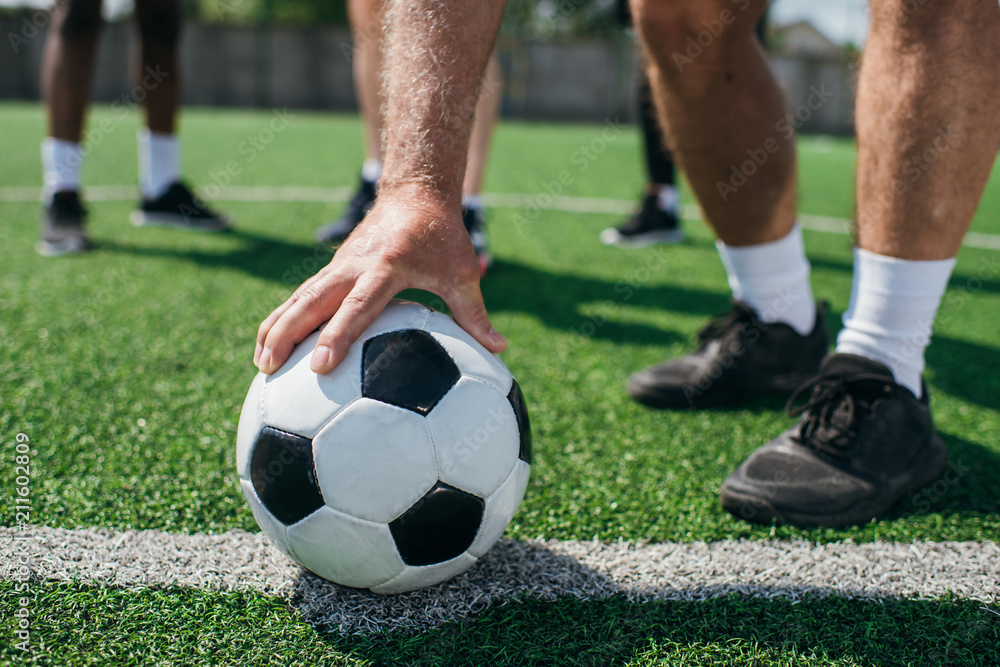 partial view of old player holding football ball with multiracial friends behind on football field