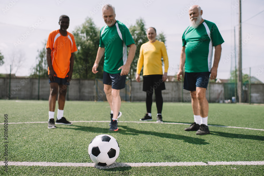 Obraz premium selective focus of football ball and multicultural elderly men on green football field