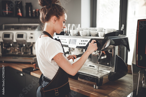 Slika na platnu Young woman barista preparing coffee using machine in the cafe