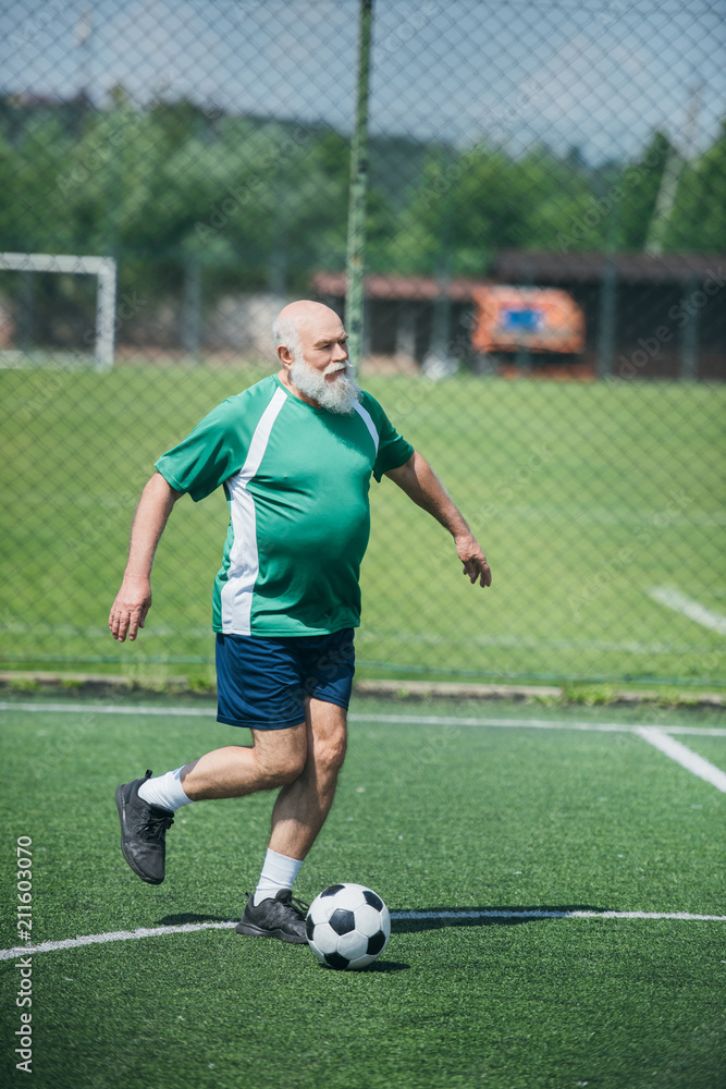 elderly bearded man playing football on field on summer day elderly bearded man playing football on field on summer day