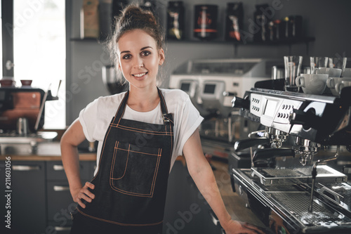 Young smiling cafe business owner standing at bar in coffee shop