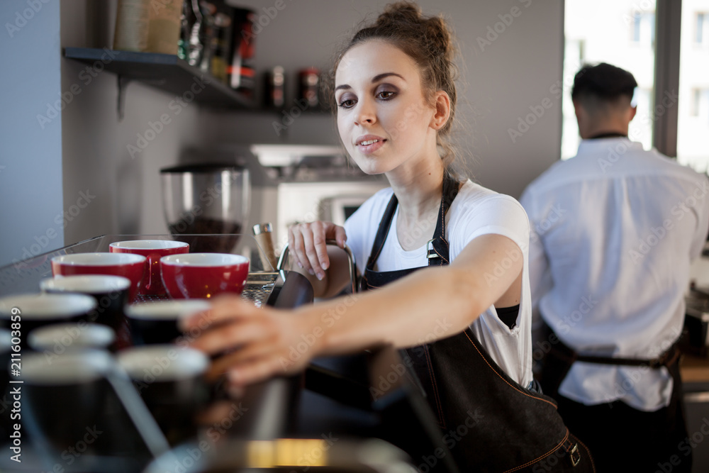 Professional female barista in apron prepares coffee at cafe