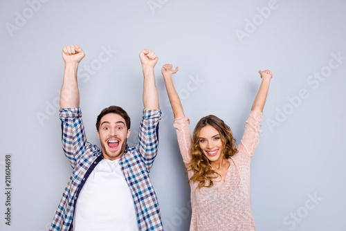 Finish! Portrait of glad positive couple in casual outfits with raised arms celebrating victory isolated on grey background