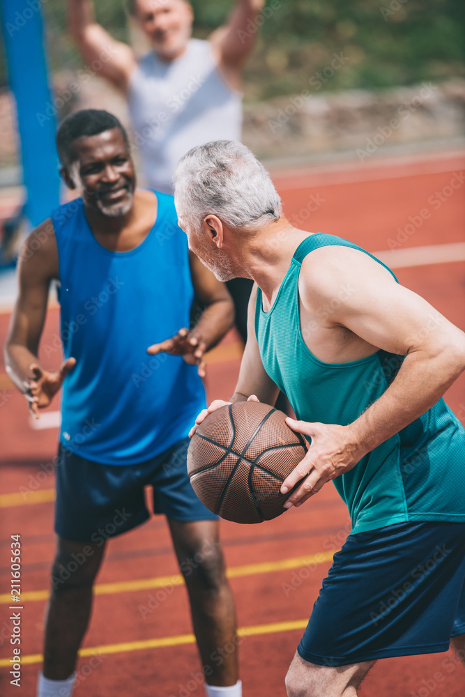 multiracial elderly men playing basketball together on playground on summer day