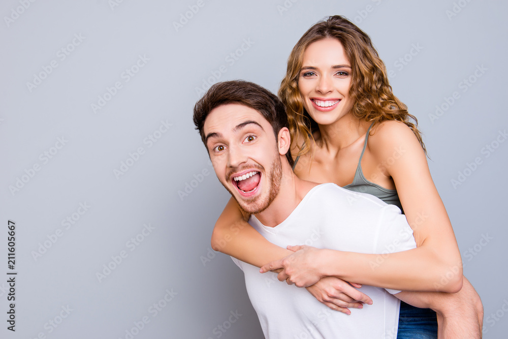 Portrait with copy space empty place of cheerful positive couple, amazed man carrying on back pretty toothy woman isolated on grey background. Advertisement concept Portrait with copy space empty place of cheerful positive couple, amazed man carrying on back pretty toothy woman isolated on grey background. Advertisement concept