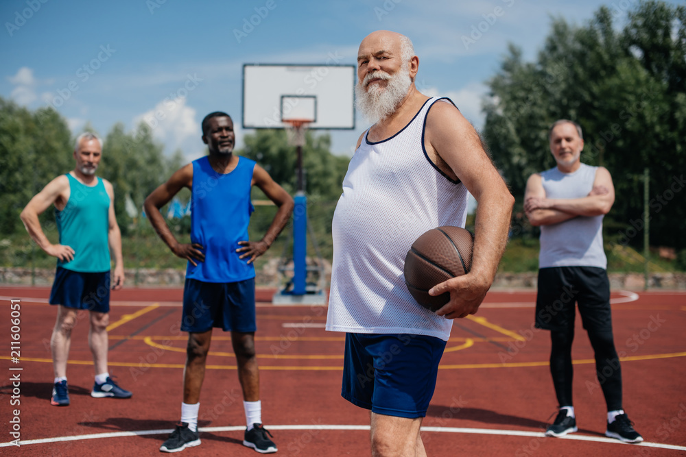selective focus of multiethnic elderly sportsmen with basketball ball on playground