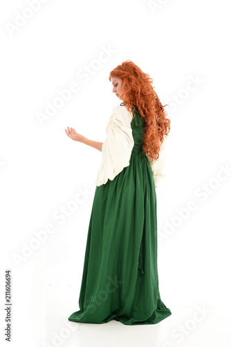 full length portrait of red haired girl wearing long green gown . standing pose with back to the camera  isolated on white studio background.