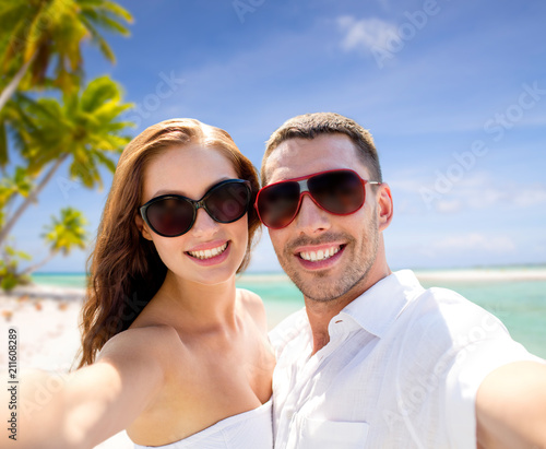 travel, tourism and summer vacation concept - smiling couple wearing sunglasses making selfie over tropical beach background in french polynesia