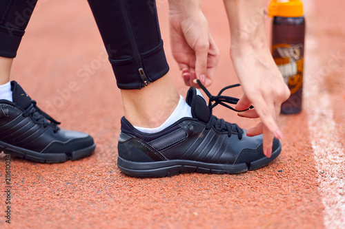 runner woman tying running shoes laces getting ready for race on run track stadium with bottle of water