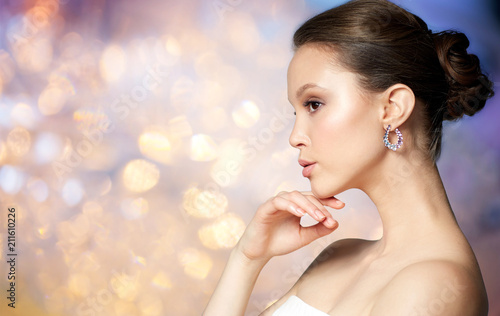 beauty, jewelry, people and luxury concept - close up of beautiful asian woman face with earring over holidays lights background