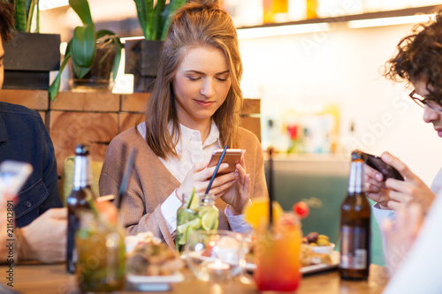 leisure, people and technology concept - happy friends with smartphones eating and drinking at restaurant