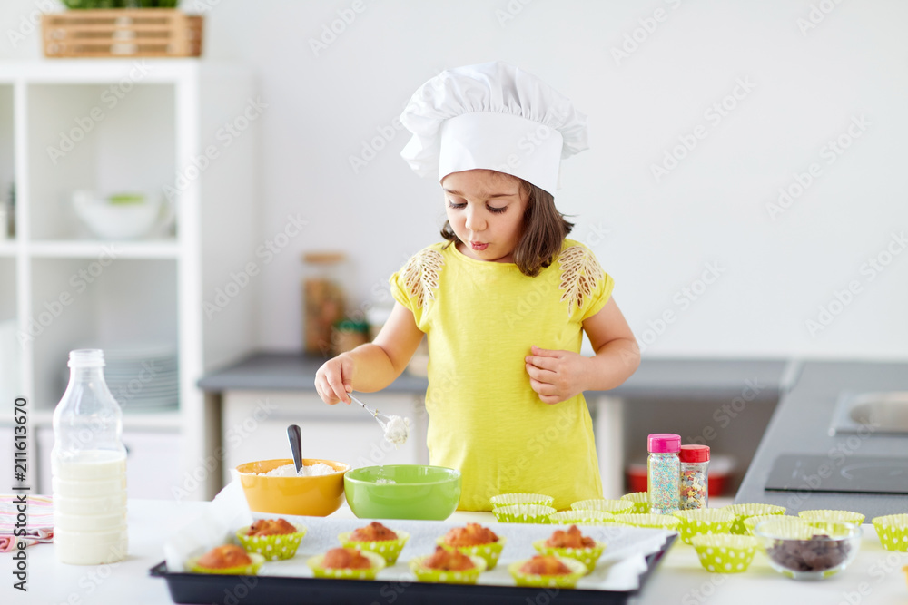 family, cooking, baking and people concept - little girl in chefs toque making batter for muffins or cupcakes at home kitchen family, cooking, baking and people concept - little girl in chefs toque making batter for muffins or cupcakes at home kitchen