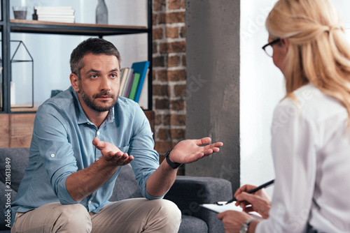 Valokuva mature man with wide arms talking to female psychiatrist at her office