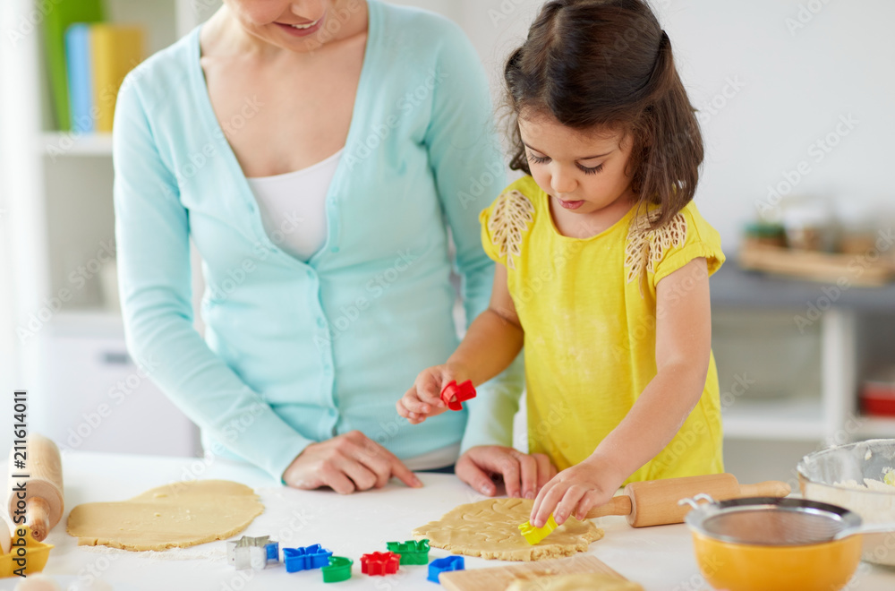 Fototapeta premium family, cooking and people concept - happy mother and little daughter with molds making cookies from dough at home kitchen