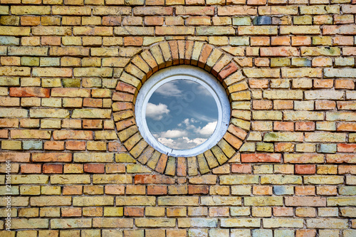 sky with clouds reflected in a round window on brick wall