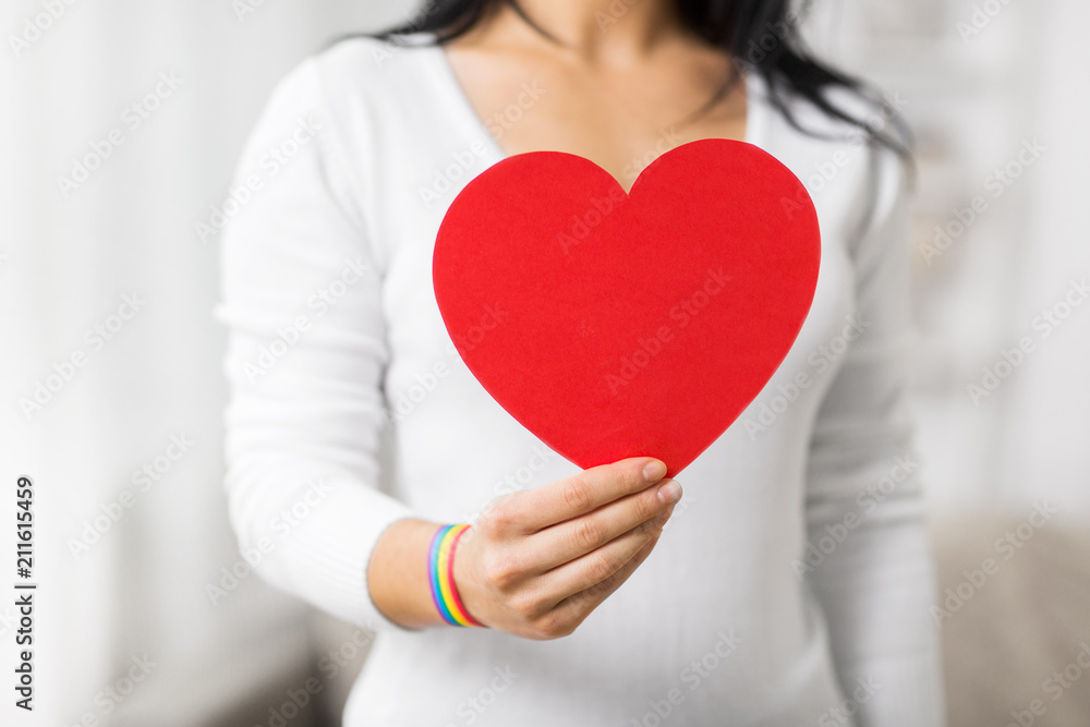 homosexual and lgbt concept - woman holding red heart shape and wearing gay pride awareness ribbon wristband homosexual and lgbt concept - woman holding red heart shape and wearing gay pride awareness ribbon wristband
