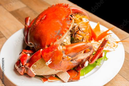 Steamed crab or Boiled crab fresh with crab's spawn in white dish showing the delicious crab's eggs inside its shell on wood table. Thai seafood.