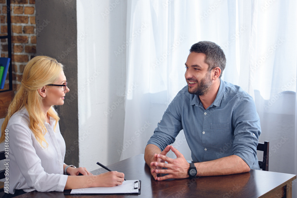 smiling man talking to female psychiatrist while she writing in clipboard at office smiling man talking to female psychiatrist while she writing in clipboard at office