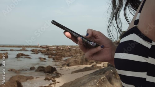 girl uses a mobile phone on the beach on the background of the sea and stones. writes a message.