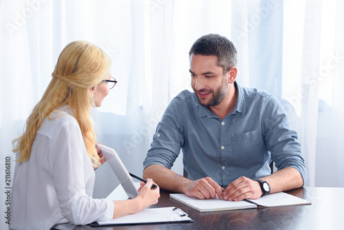 Wallpaper Mural side view of female counselor pointing on digital tablet screen by pen to smiling male patient at table in office Torontodigital.ca