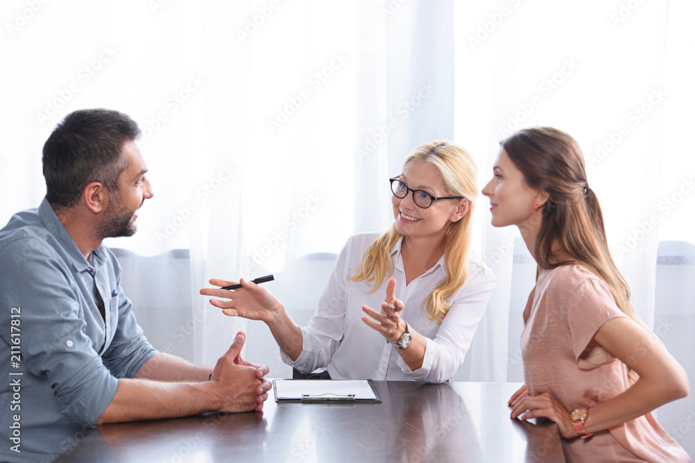 smiling female counselor gesturing by hands and talking to couple on therapy session in office smiling female counselor gesturing by hands and talking to couple on therapy session in office